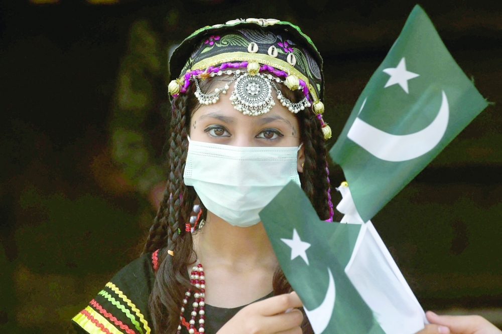 A girl poses with flags of Pakistan at the tomb of national poet Allama Mohammad Iqbal during Pakistan's 75th Independence Day celebrations in Lahore on Saturday. -- AFP