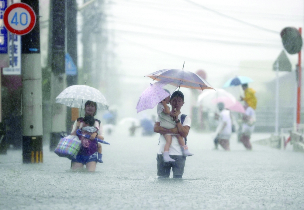 Local residents walk in a road flooded by heavy rain in Kurume, Fukuoka prefecture on Saturday. -- Reuters