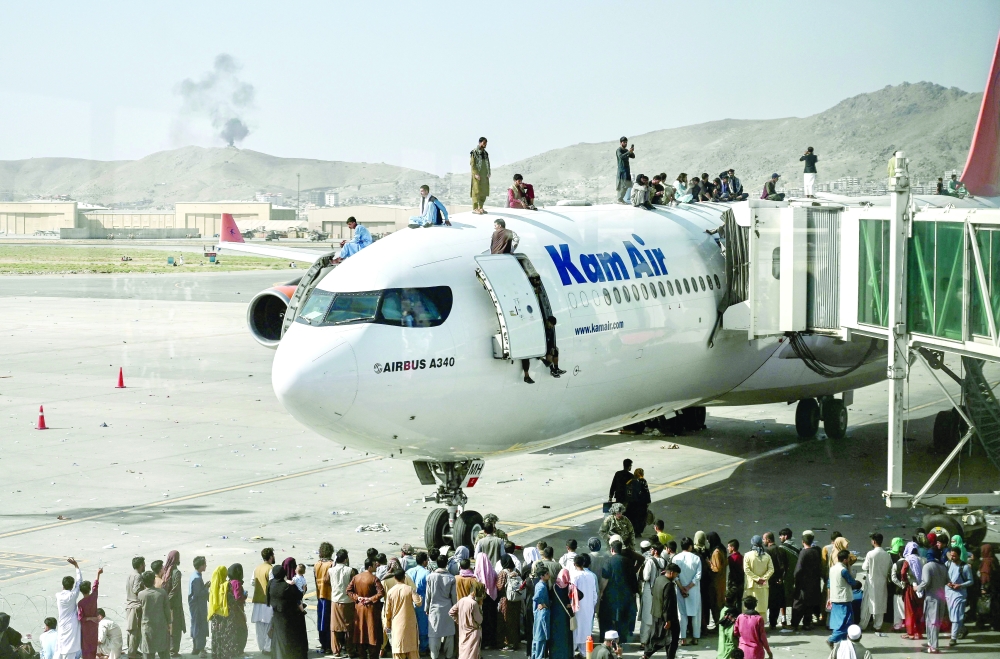 Afghan people climb atop a plane as they wait at the Kabul airport on Monday. -- AFP