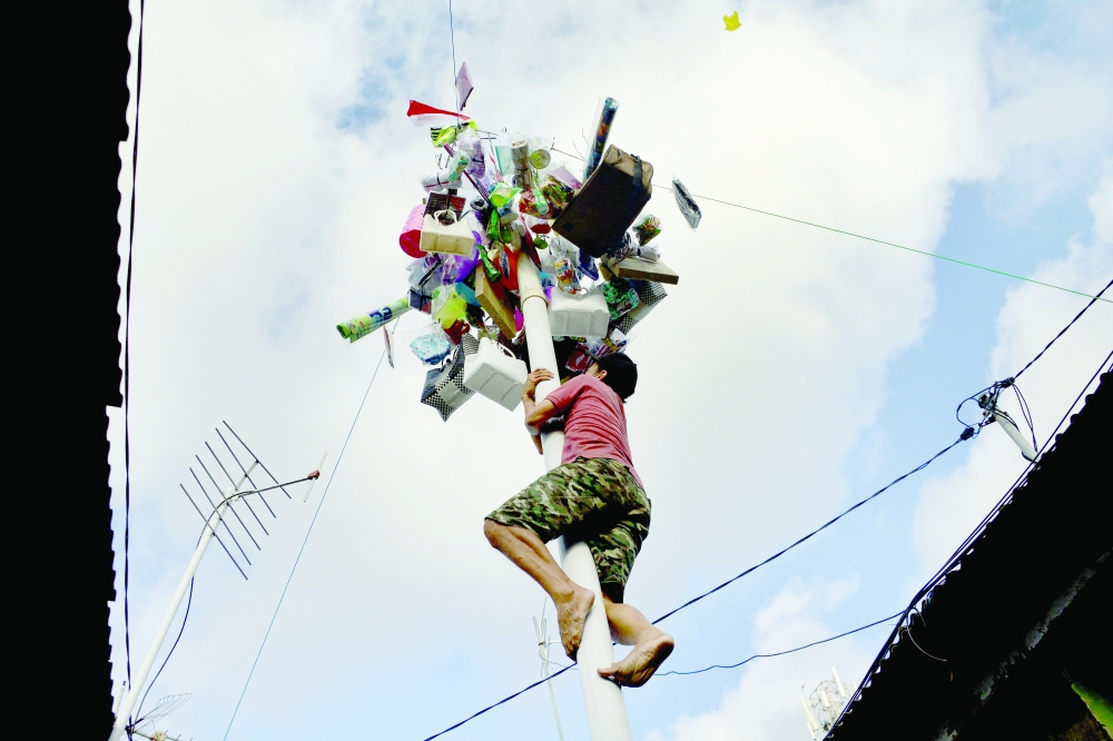 A man climbs to the top of a pole on which prizes and other items are attached as part of festivities celebrating Indonesia's 76th Independence Day in Denpasar on Bali island, on Tuesday. - AFP