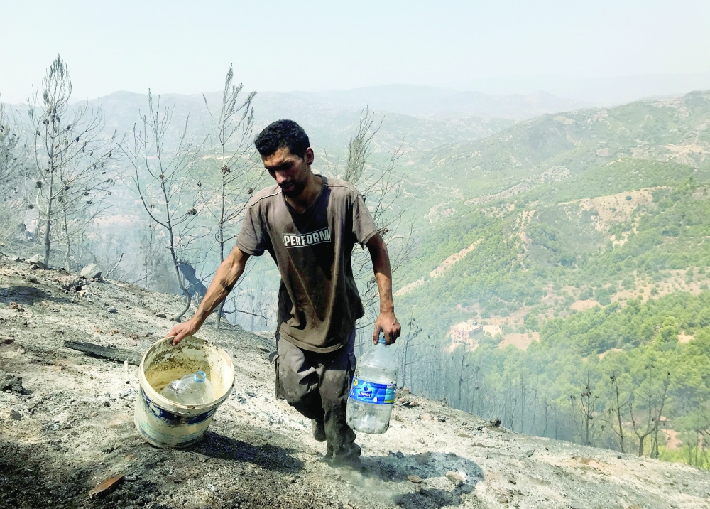 A man carries water containers as he works with others to douse hotspots in an area hit by a wildfire in El Bir village, Bejaia province, on Tuesday. -- Reuters
