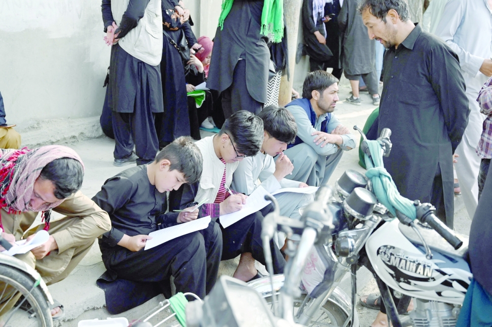  Afghan people fill up their details on a sheet of paper to register their name in order to leaves the country in front of the British and Canadian embassy in Kabul. - AFP


