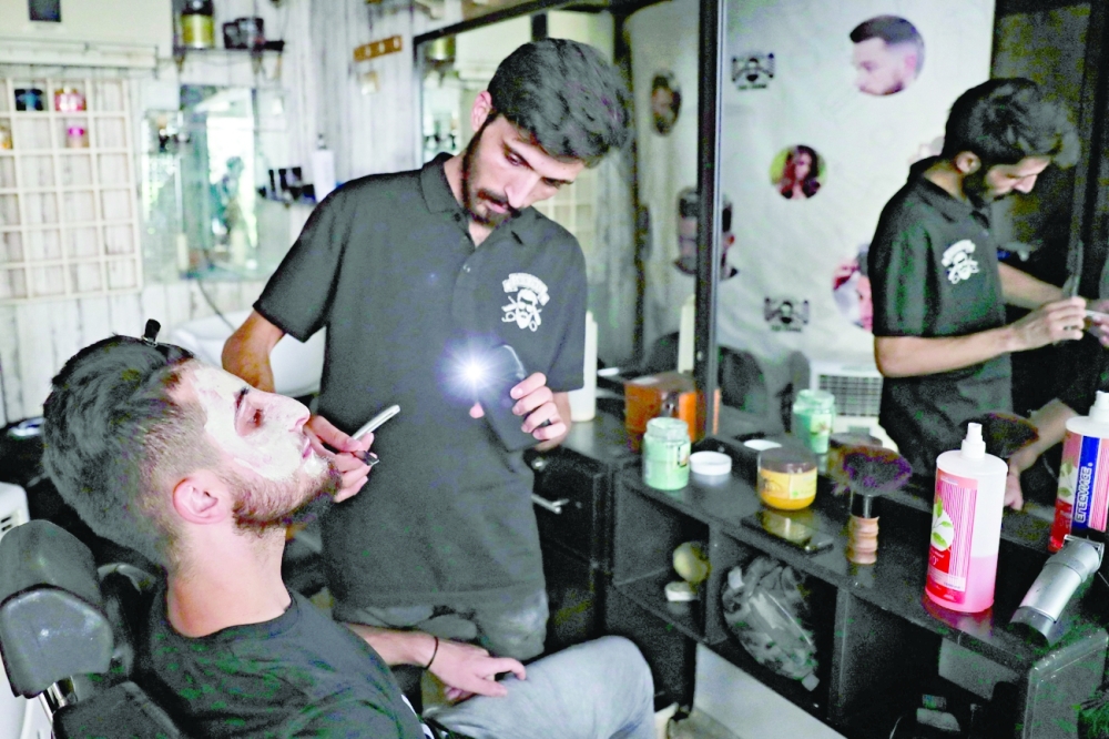 A barber uses flashlight of his phone as he shaves a customer at his shop in Beirut. -- AFP

