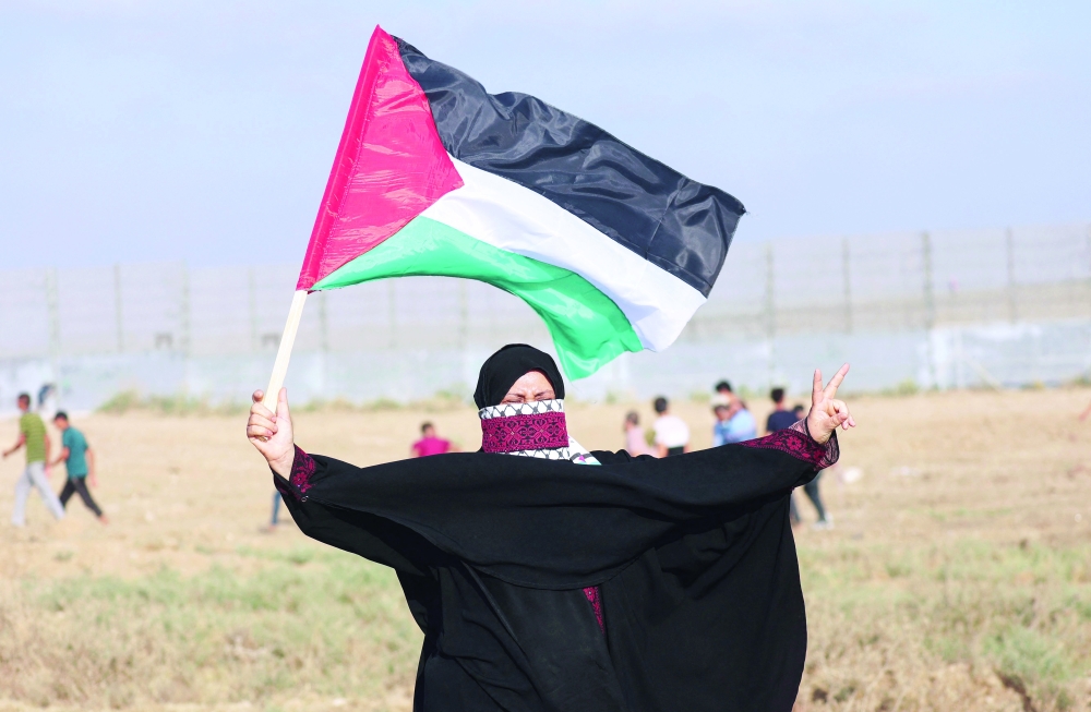 A Palestinian protester with the national flag as she takes part in a demonstration by the border fence with Israel, east of Gaza City, denouncing the Israeli siege of the Palestinian strip, on Saturday. -- AFP