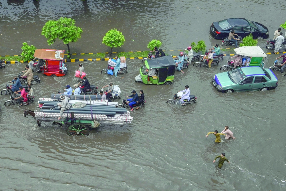 Commuters make their way through a flooded street after heavy monsoon rains in Lahore, Pakistan, on Saturday. - AFP