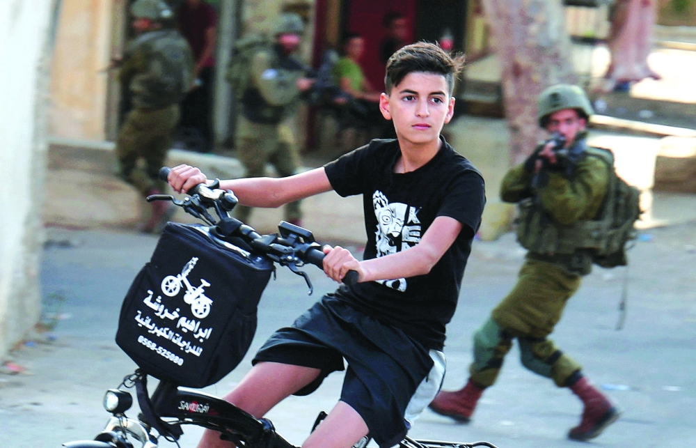 A Palestinian boy rides as bicycle as Israeli soldiers patrol the village of Salem, east of Nablus on Tuesday. -- AFP