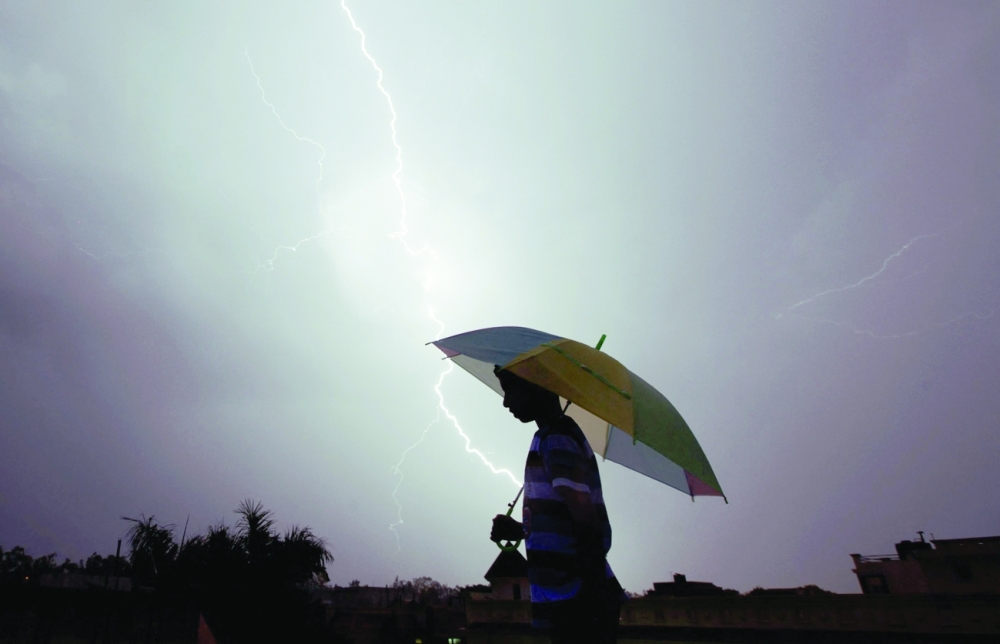 A pedestrian walking with an umbrella as lightning strikes during an evening thunderstorm in Jammu. -- AFP
