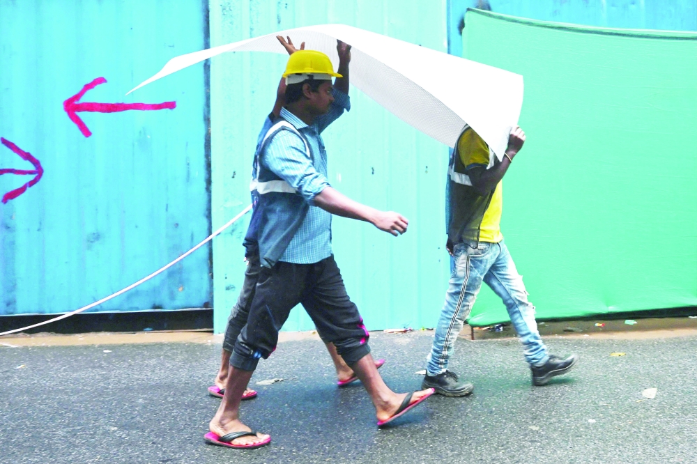 Construction workers use a plastic sheet to shelter during a heavy rainfall in New Delhi. - AFP