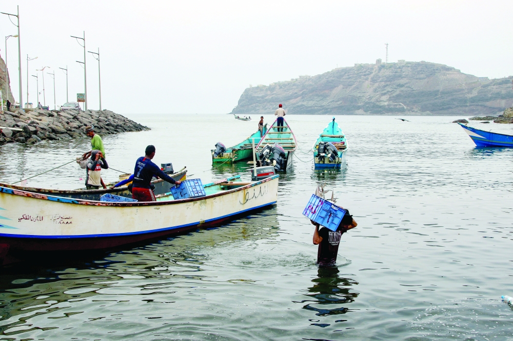 A fisherman carries a box of fish after returning from a fishing trip in Aden, Yemen. - Reuters