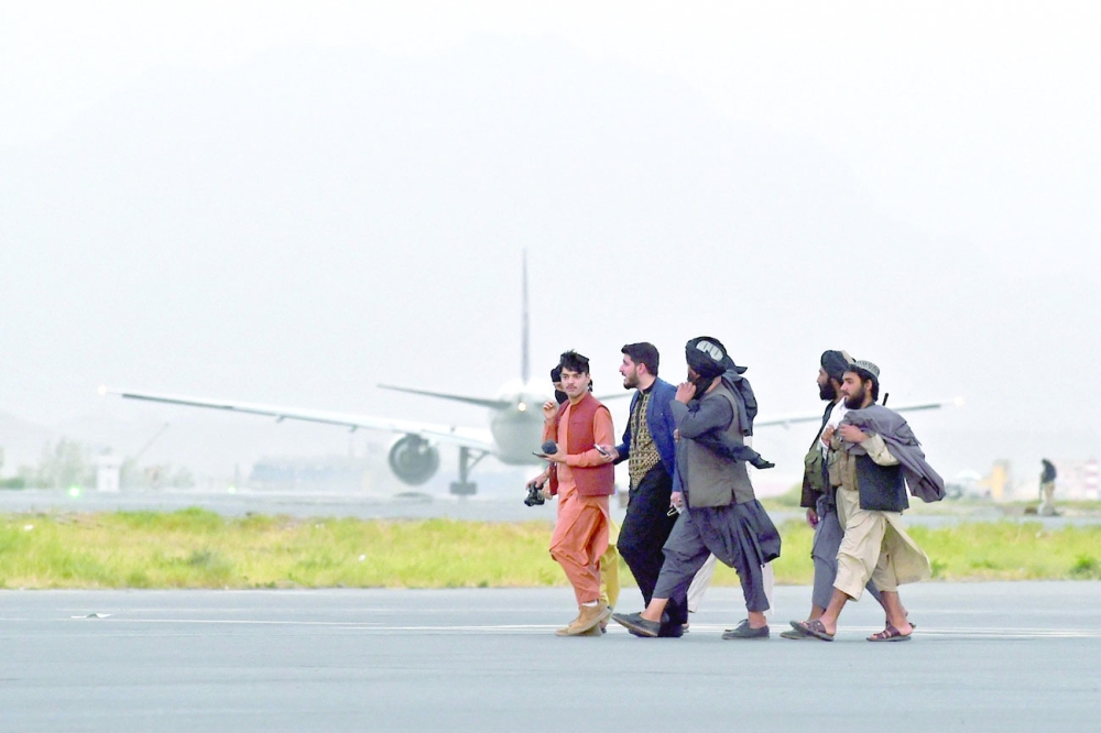 Taliban fighters walk past a Qatar Airways aircraft preparing to take off from the airport in Kabul. -- AFP
