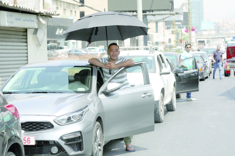 A man shields from the sun with an umbrella as he waits to get fuel from a gas station in Jal el-Dib. -- Reuters