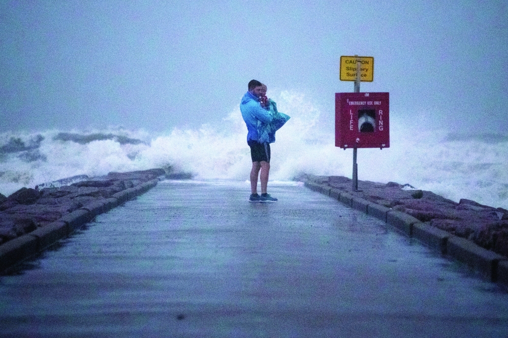 Local resident John Smith holds his 18-month-old son Owen as he stands near breaking waves on a pier ahead of the arrival of Tropical Storm Nicholas in Galveston, Texas. - Reuters
