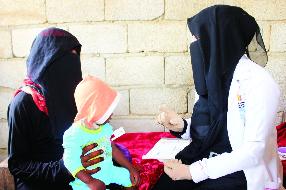 Volunteer health worker Ashwaq Mahmoud talks to a mother as she assesses her child's nutritional status in Abs. - Reuters