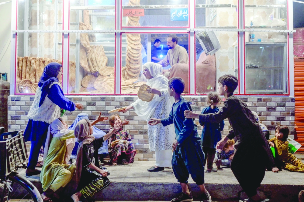 A woman gives bread to young people in need in front of bakery in Kabul on Sunday. - AFP