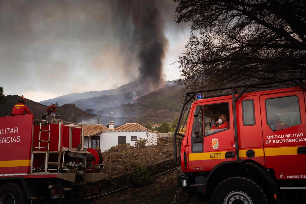 Firefighters stand next to houses in the residential area of Los Campitos at Los Llanos de Aridane, on the Canary Island of La Palma on September 20, 2021. 