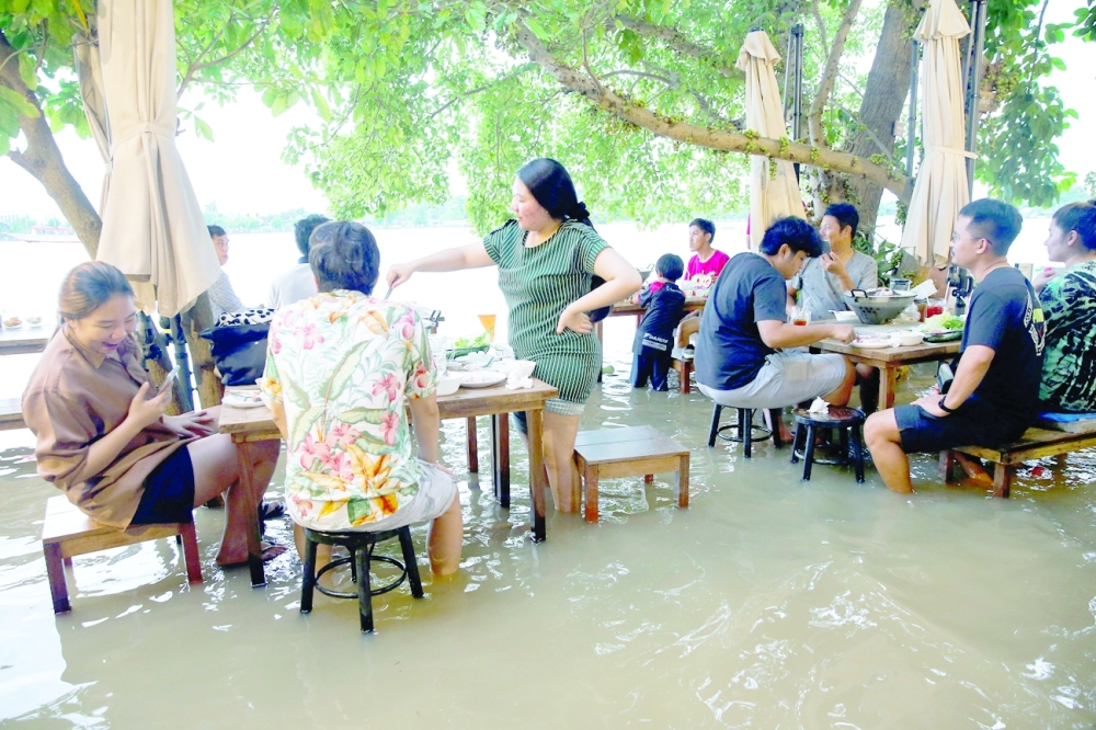 People eat at a flooded restaurant, where patrons stand up from their tables every time the waves come in, on a river bank in Nonthaburi near Bangkok. -- Reuters
