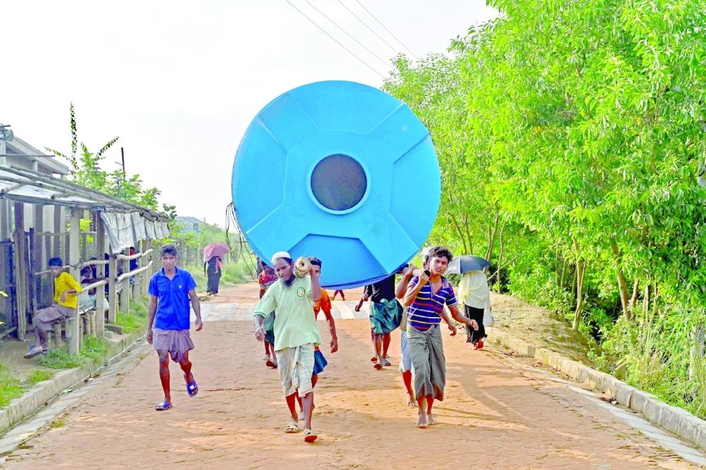 Rohingya refugees carry a water tank at Kutupalong refugee camp in Ukhia. Some 19,000 refugees from Myanmar have already relocated from crowded camps on the mainland to Bhashan Char island. -- AFP
