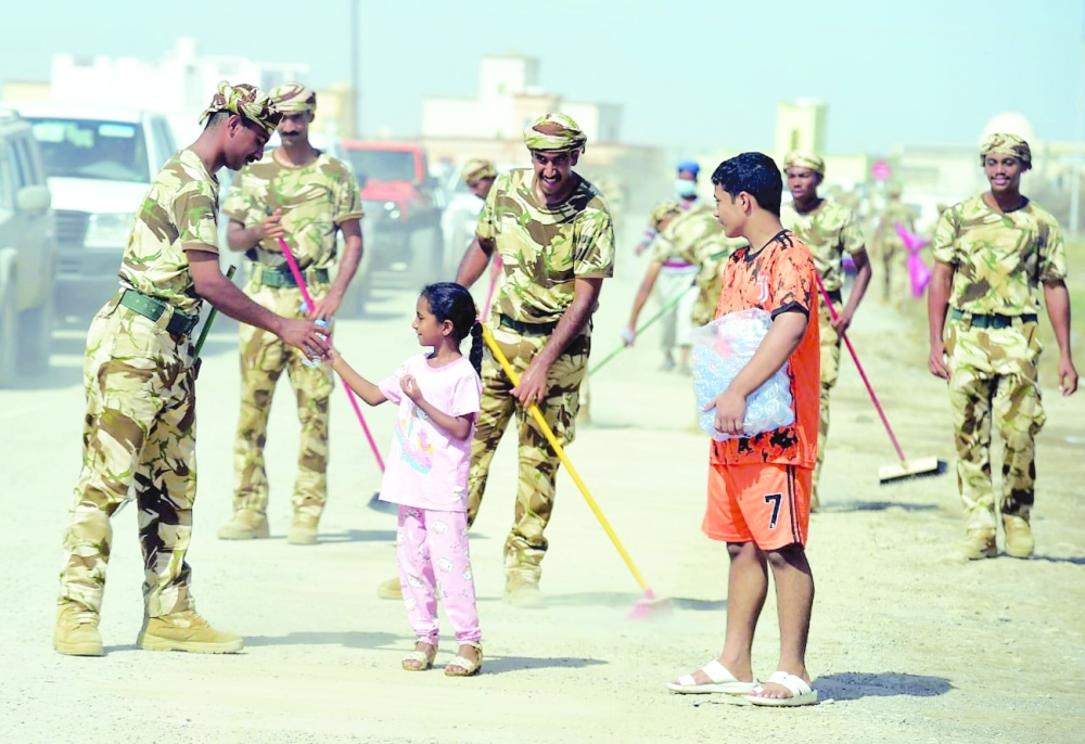 A defense personnel offer water bottle to a girl in Al Khaburah on Friday. -- ONA