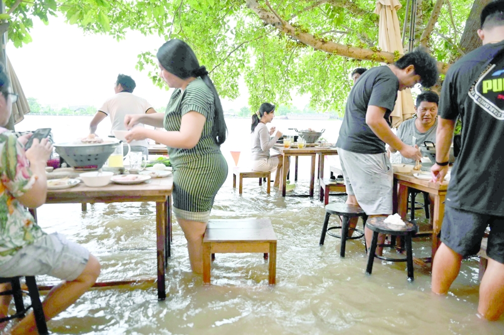 People eat at a flooded restaurant, where patrons stand up from their tables every time the waves come in, on a river bank in Nonthaburi near Bangkok. -- AFP