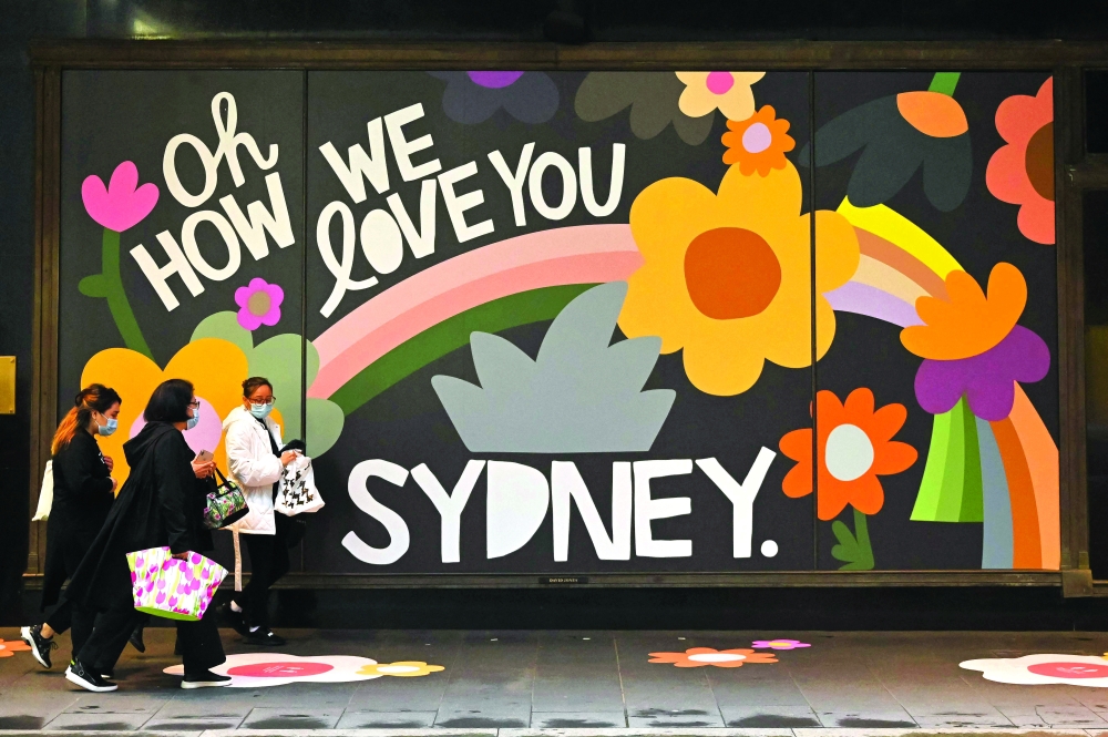 People carrying shopping bags walk past a retail store in Sydney as the city ended their lockdown against the coronavirus after 106 days. - AFP

