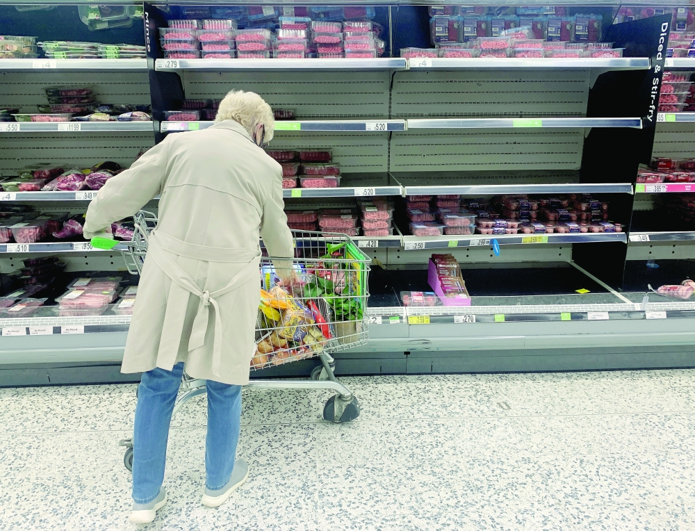 A shopper stands in front of empty shelves in the meat aisle of a supermarket in Liverpool