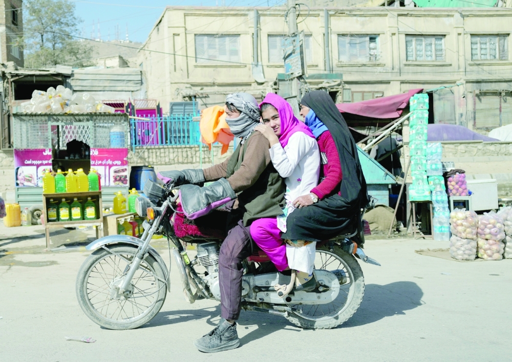 An Afghan family rides a motorcycle past roadside shops in Kabul on Saturday. -- Reuters
