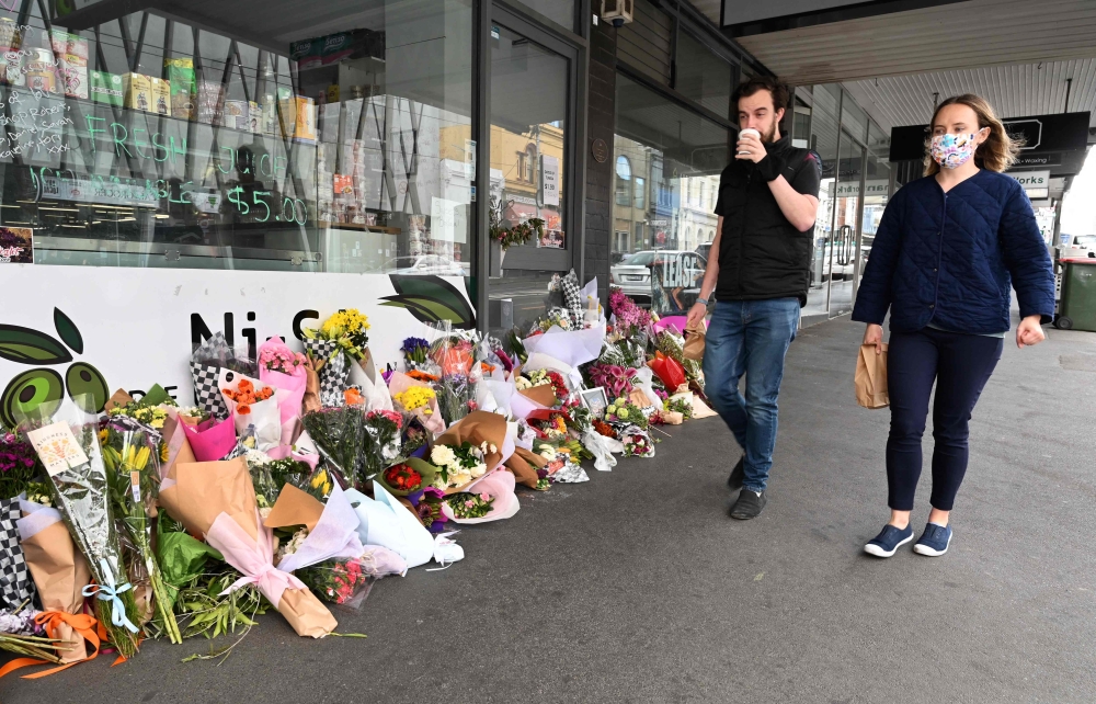 People walk past a floral tribute to a popular delicatessen owner who died from Covid-19 in Melbourne during a lockdown against Covid-19 coronavirus as Sydney ended a 106-day lockdown. 