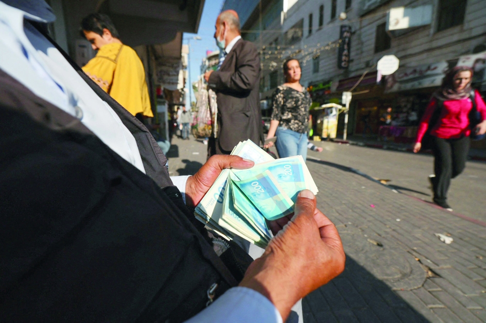 A Palestinian man counts a stack of Israeli Shekels in the West Bank city of Ramallah. - AFP