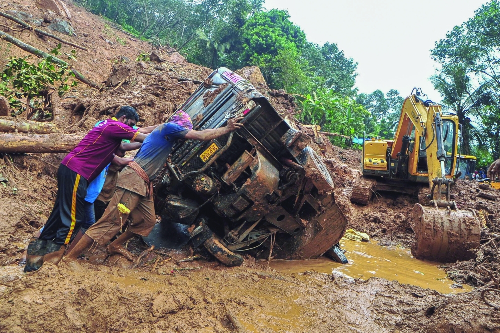 Rescue workers push a overturned vehicle stuck in the mud and debris at a site of a landslide claimed to be caused by heavy rains in Kokkayar in Kerala on Sunday. - AFP