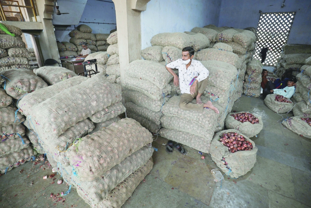A vendor sits on the sacks of onion as he waits for customers at a vegetable market in Ahmedabad. - Reuters