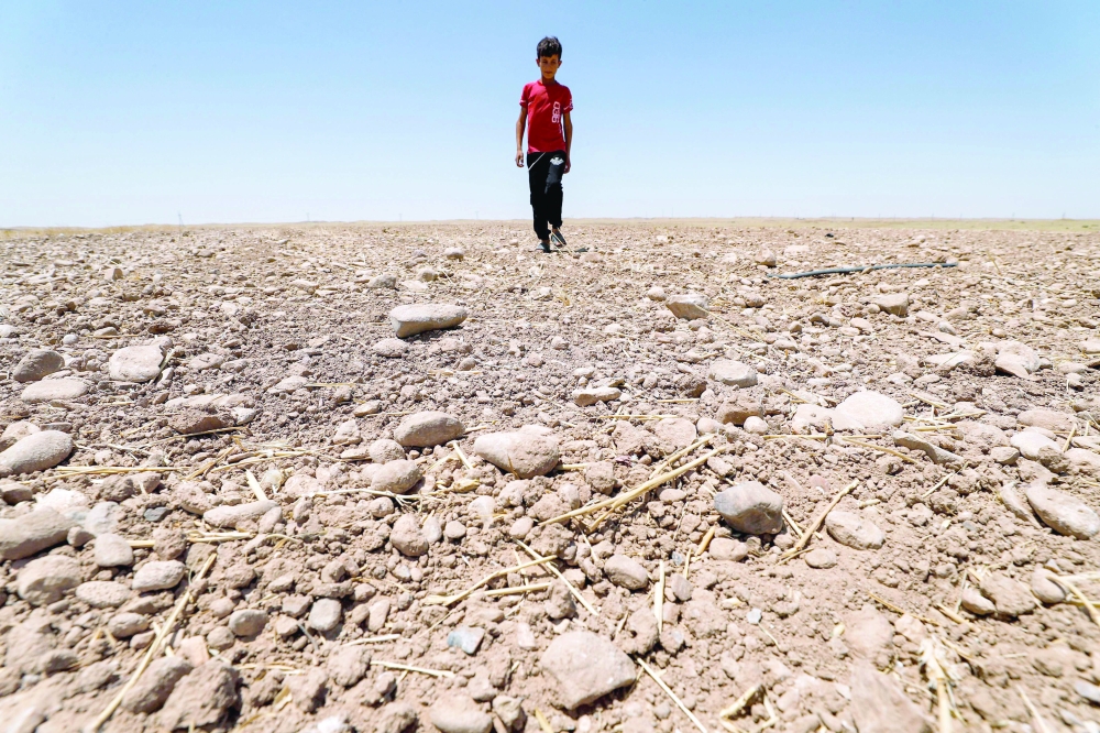 (FILES) In this file photo taken on June 24, 2021, a boy walks through a dried up agricultural field in the Saadiya area, north of Diyala in eastern Iraq. The climate crisis threatens a double blow for the Middle East, experts say, by destroying its oil income as the world shifts to renewables and raising temperatures to unlivable extremes. (Photo by AHMAD AL-RUBAYE / AFP)
