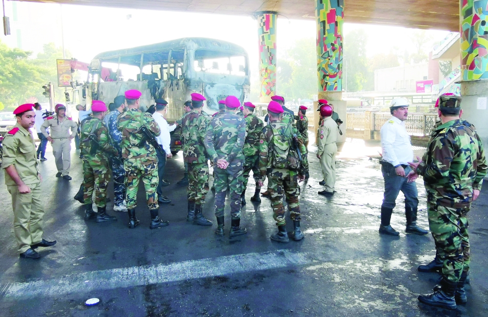 Syrian security forces stand guard as the charred bus is removed from the site of an early morning attack in Damascus on Wednesday. - AFP