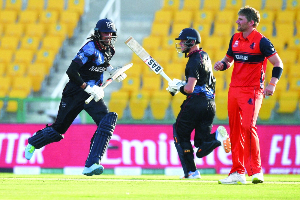 Namibia's captain Gerhard Erasmus (C) and Namibia's David Wiese (L) run between the wickets during the ICC men's Twenty20 World Cup cricket match between Namibia and Netherlands at the Sheikh Zayed Stadium in Abu Dhabi on October 20, 2021. (Photo by INDRANIL MUKHERJEE / AFP)

