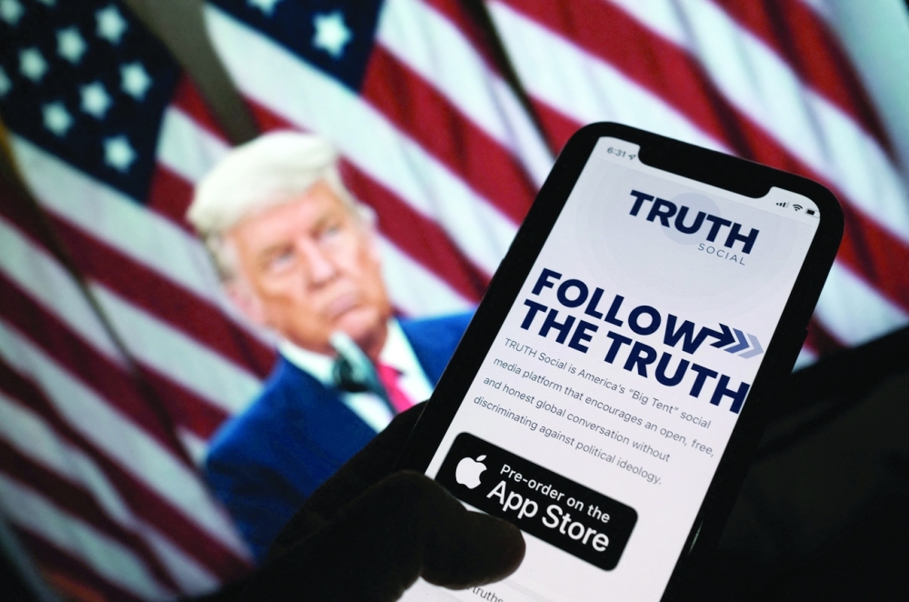 This illustration photo shows a person checking the app store on a smartphone for "Truth Social", with a photo of Donald Trump on a computer screen in the background, in Los Angeles. - AFP 