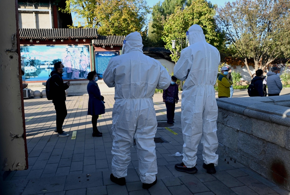 Health workers look at people queueing for swab tests for the Covid-19 coronavirus at a nucleic acid collection station in Beijing on October 26, 2021. 
