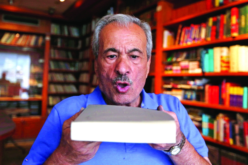 Muhammad Salem al Nouri blows dust off a book at the Dar al Maarifa library in Damascus. - AFP