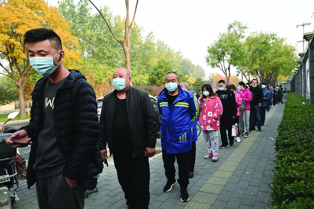 People wait in line to receive Covid-19 vaccination booster shots along a street in Beijing on Saturday. - AFP