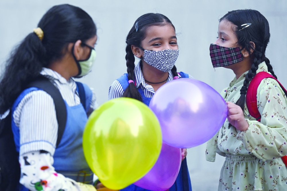 Children hold balloons as they enter their school in New Delhi on Monday. - AFP