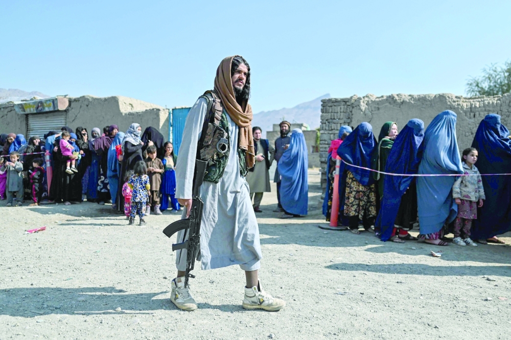 A Taliban fighter walks next to women waiting in line during a World Food Programme food distribution on the outskirts of Kabul on Saturday. - AFP