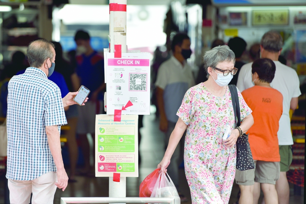 People entering a food centre check-in with their phones before they are allowed to dine-in in Singapore. - Reuters