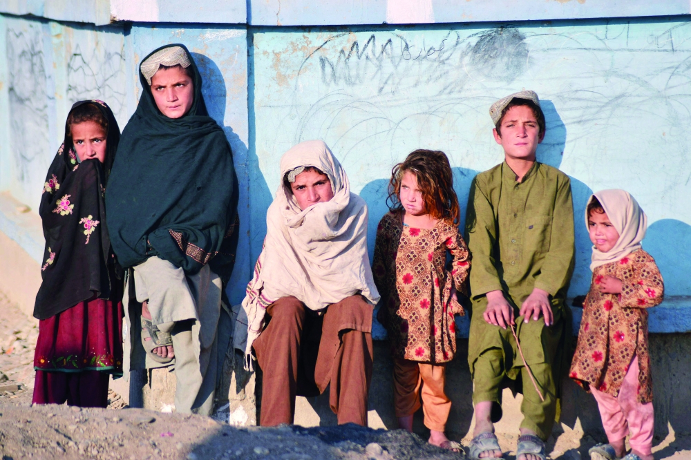 Children bask in the sun next to a wall along a street in Nad Ali district, Helmand province, Afghanistan, on Wednesday. - AFP