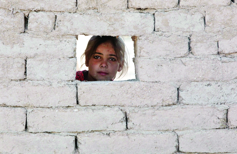 A Syrian girl looks out of a hole in a newly-built mudbrick house in a village erected east of Al Safira in the countryside of Jarabulus, Aleppo province. - AFP