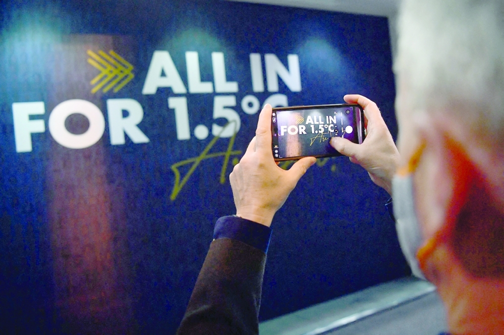 A man takes pictures of a wall reading "All in for 1.5C" during the COP26 Climate Change Conference in Glasgow on Thursday. -- AFP