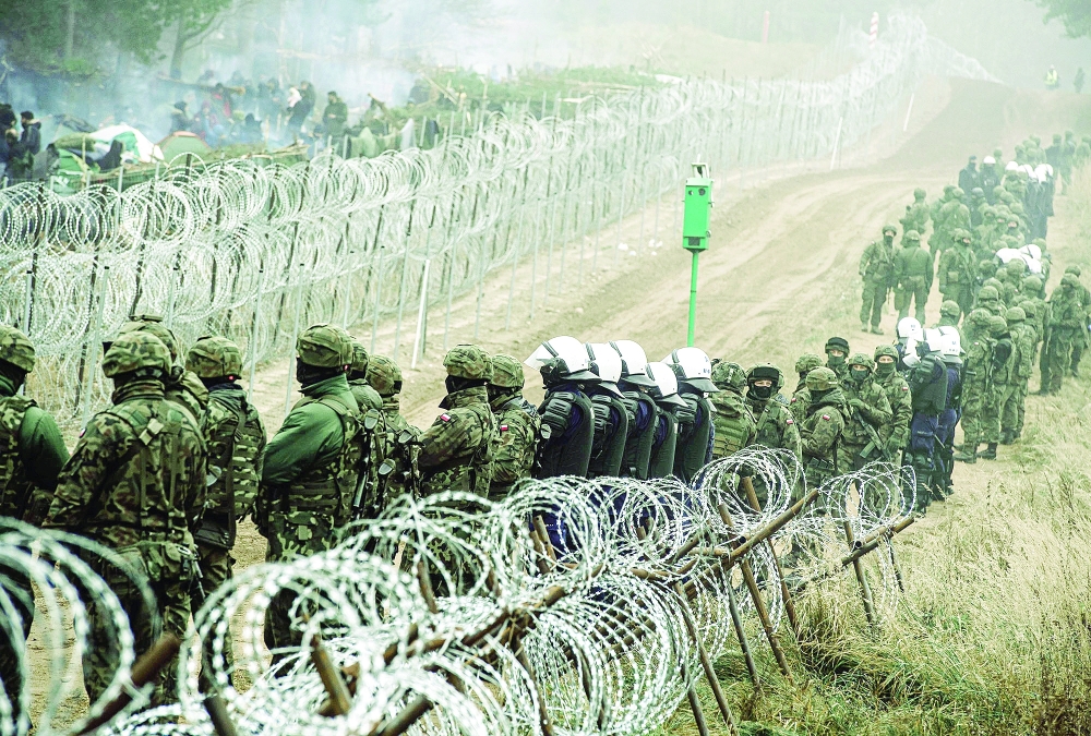 Polish soldiers and police watch migrants at the Poland-Belarus border near Kuznica, Poland, in this photograph released by the Territorial Defence Forces, on Friday. - Reuters