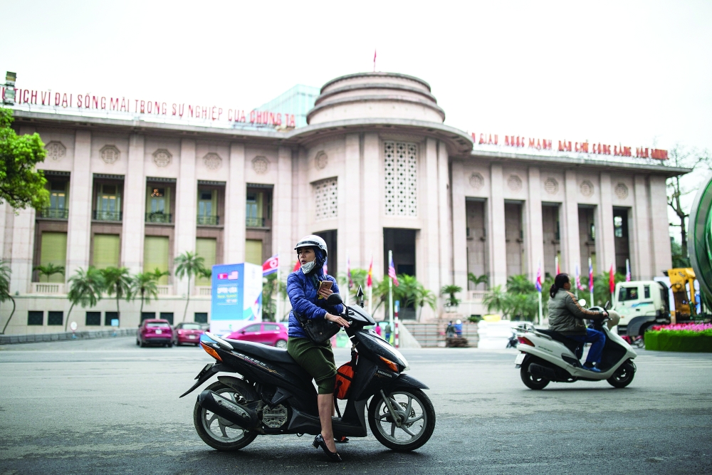 Motorists ride a motorcycle past the State Bank of Vietnam building in Hanoi. — Reuters