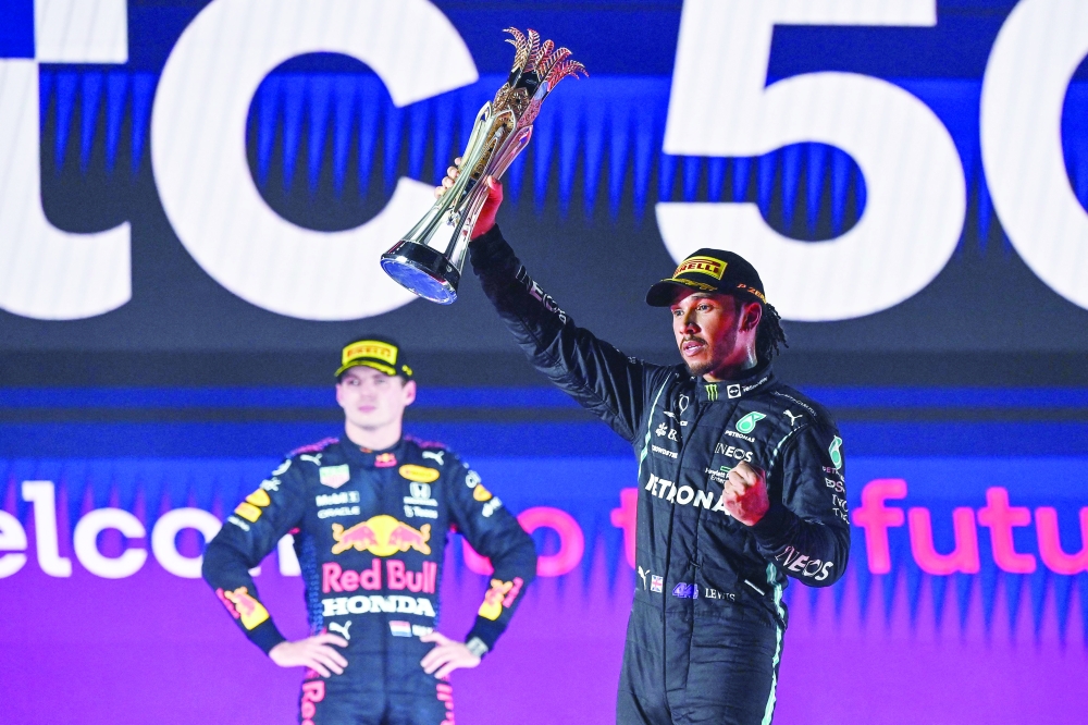 Mercedes' driver Lewis Hamilton (R) reacts with his trophy flanked by second-placed Red Bull driver Max Verstappen (L) during the podium ceremony after the Saudi Arabian Grand Prix at the Jeddah Corniche Circuit. -- AFP
