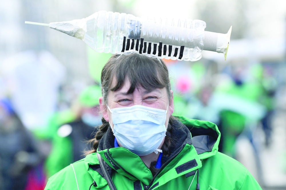 A health care worker carries a symbolic syringe shaped item on her head as she participates in a trade union demonstration against their mandatory anti-Covid 19 vaccination in Brussels. - AFP

