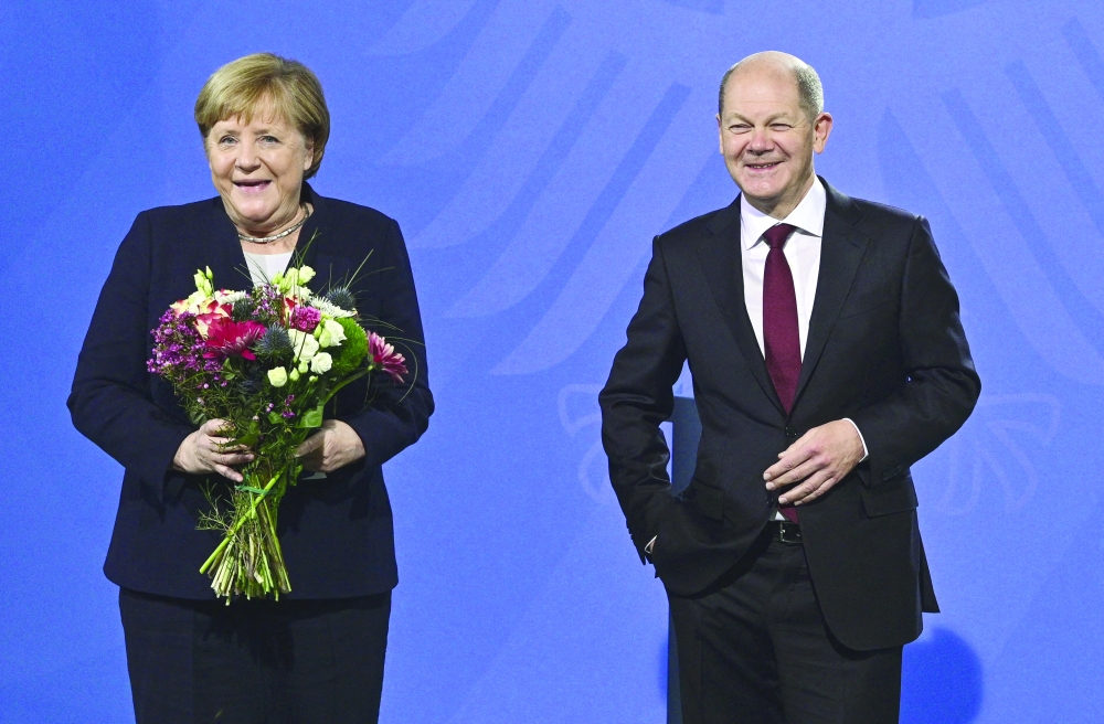 German Chancellor Olaf Scholz and his predecessor Angela Merkel pose after Scholz gave Merkel a bouquet of flowers during a handover ceremony in Berlin. - AFP