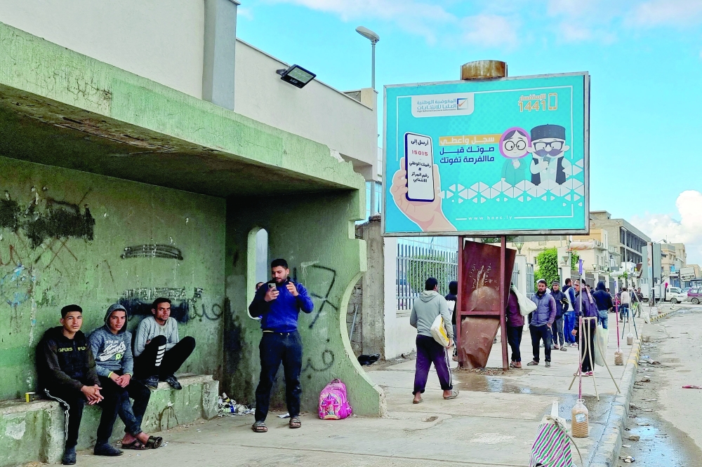 Workers walk by an electoral billboard reading in Arabic "register and vote before missing your chance" in Libya's capital Tripoli on Tuesday. - AFP 