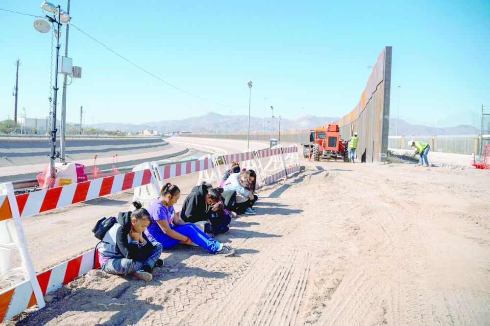 Salvadoran migrants wait for a transport to arrive after turning themselves into US Border Patrol, near the border wall under construction in El Paso, Texas.  -- AFP